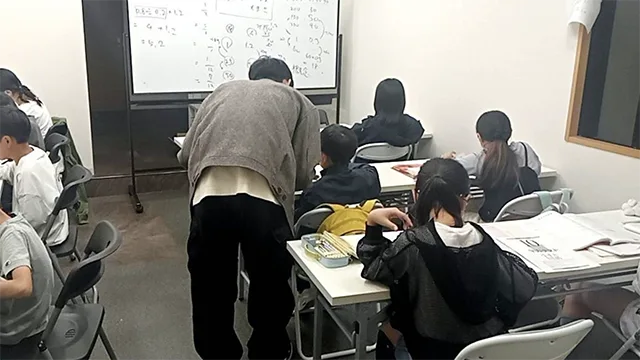 生徒の机の横で、講師がかがんで教えている教室の様子